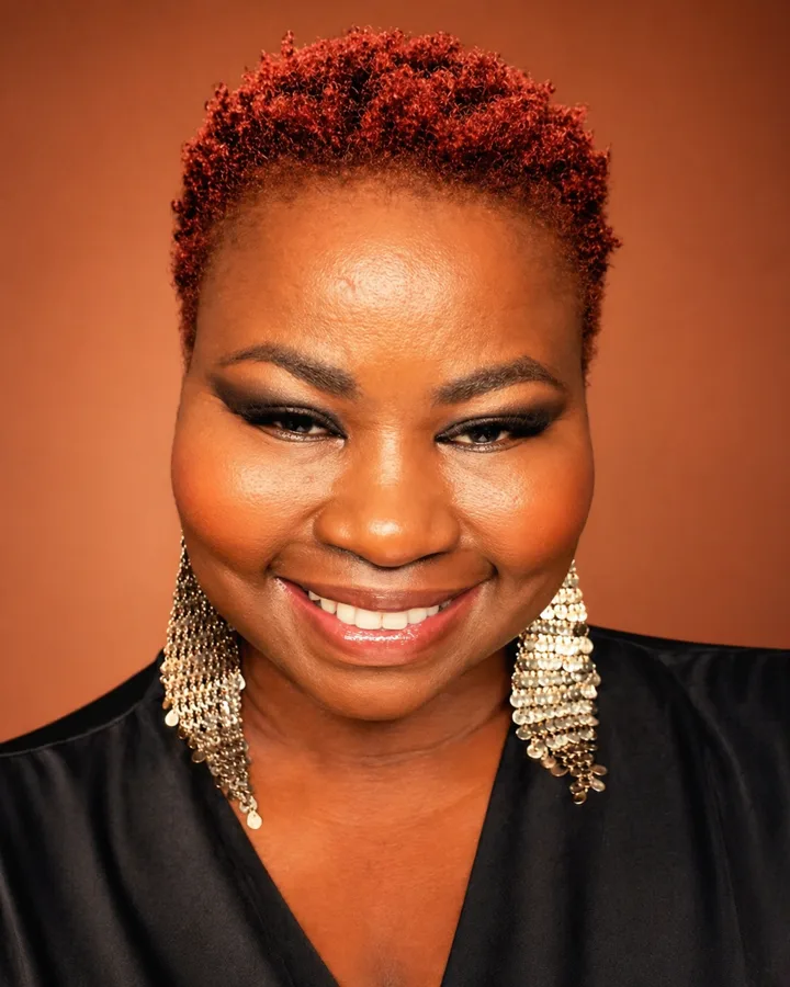 Fleur Anderson, fondatrice de JATTENDS, souriante, cheveux courts roux, sur fond terracotta